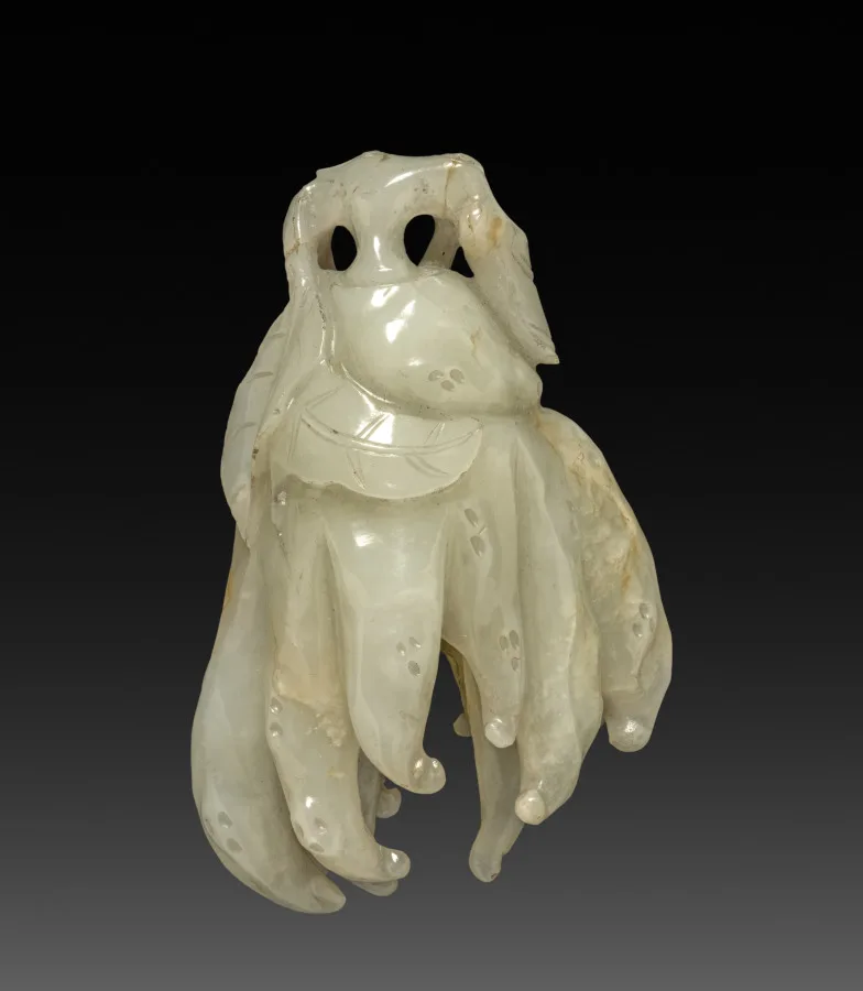 Nephrite pendant of pale green stone with carved surface and a drilled suspension hole