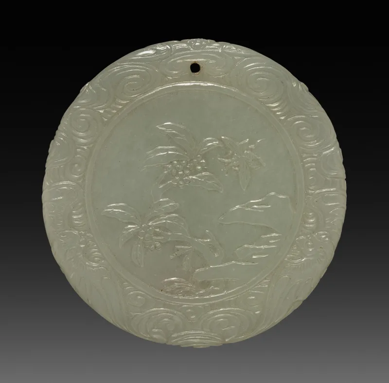 Circular nephrite pendant with carved surface decoration and a central opening