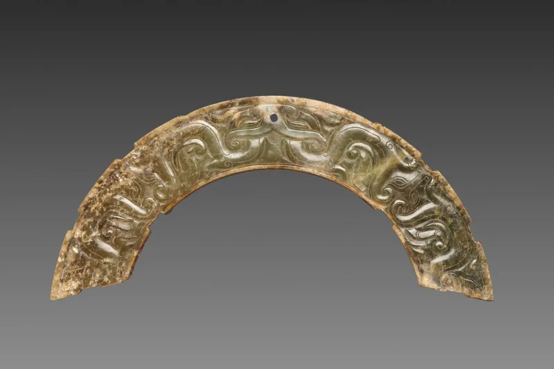 Arc-shaped nephrite pendant carved in low relief with an animal mask and interlaced ornament